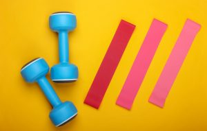 Dumbbells with fitness elastic bands on a yellow background. Top view, flat lay